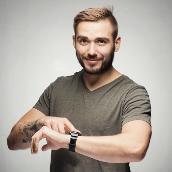 Bearded young man pointing to his watch and smiling.